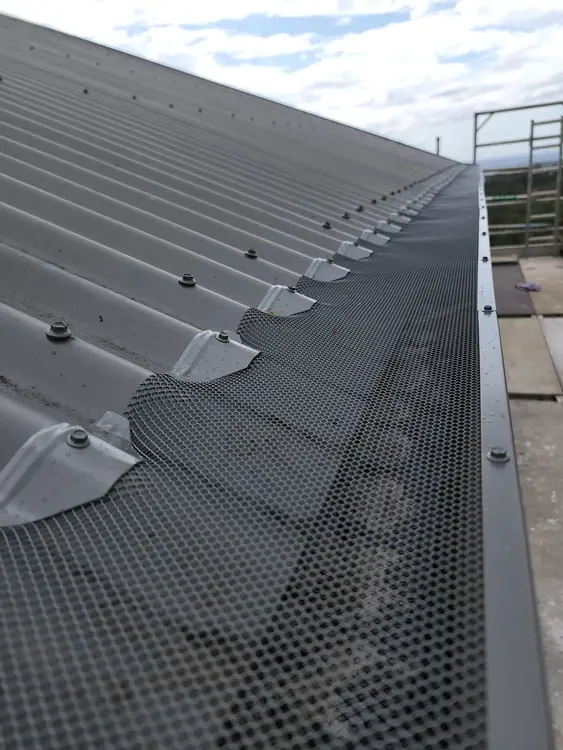 Black gutter guard mesh installed along a corrugated metal roof